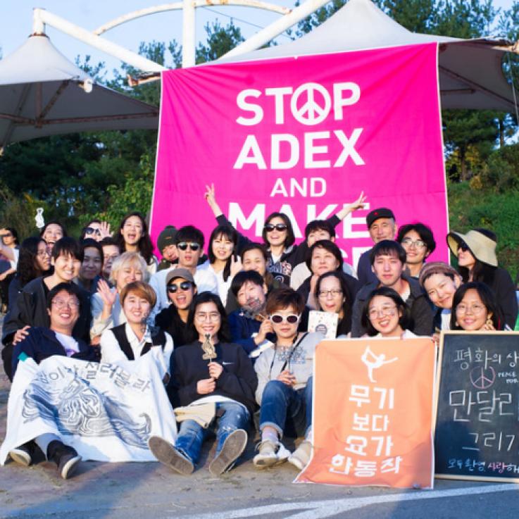 Un grupo de activistas coreanos se reúnen ante un cartel rosa que dice "stop ADEX"